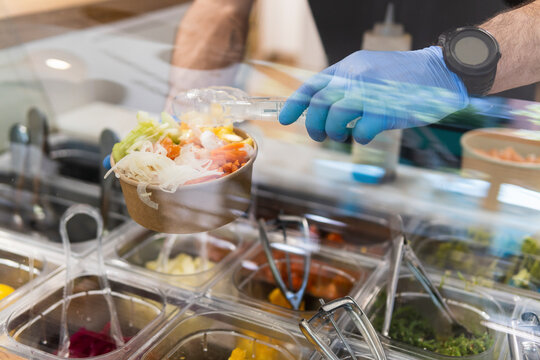 Chef with protective gloves preparing salad at food bar in restaurant
