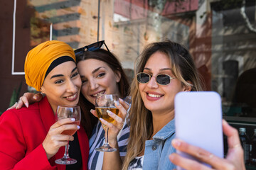 Beautiful woman taking selfie through smart phone with female friends while having drinks