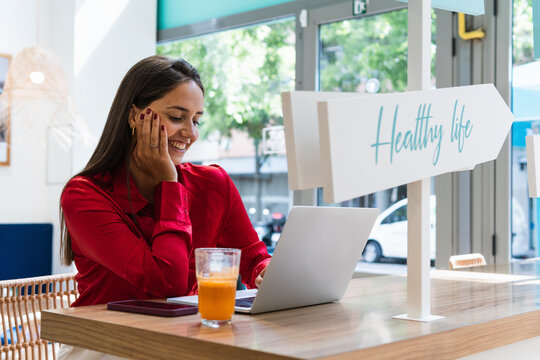 Smiling businesswoman with hand on chin using laptop at restaurant