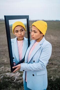 Young woman looking at reflection in mirror on field