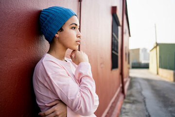 Contemplating woman with hand on chin standing in front of wall