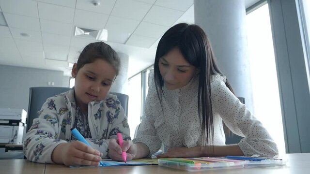 Working mom works in the office. Young woman and cute child in the office draw. Female business, kindness, care