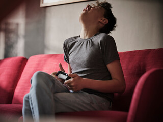 Disappointed boy with game controller on sofa at home