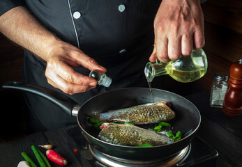 Professional chef prepares fresh fish in a pan with oil. Preparation for cooking fish food. Working environment in the kitchen of a restaurant or cafe
