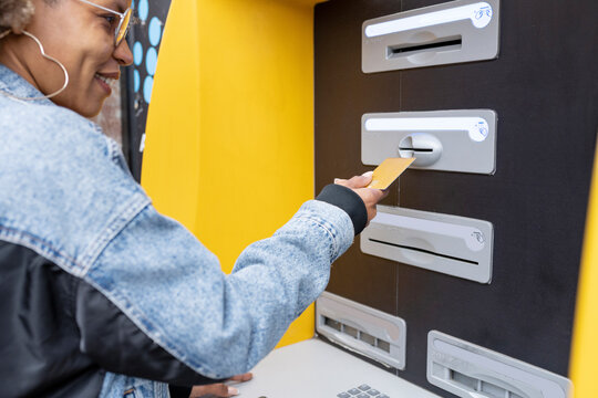 Smiling woman inserting credit card in ATM machine