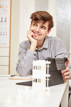 Male architect with hand on chin looking away while sitting with digital tablet at office
