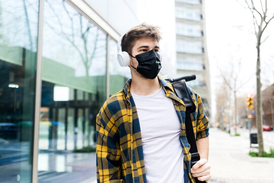 Young man wearing protective face mask while carrying an electrical scooter