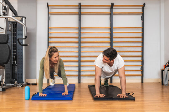Smiling male and female athletes doing push-ups on exercise mat in gym