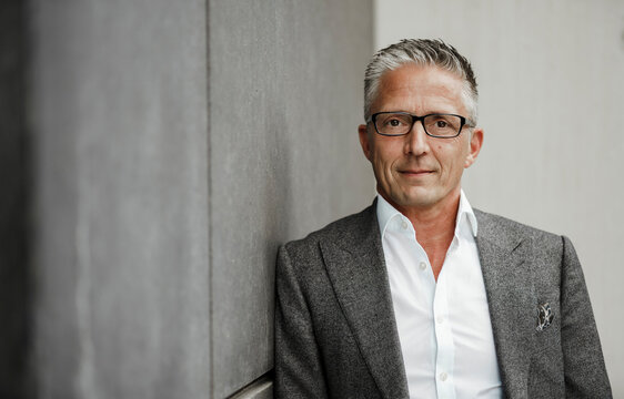 Businessman wearing eyeglasses leaning on gray wall