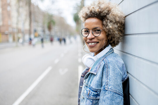Smiling mid adult woman wearing eyeglasses leaning on wall