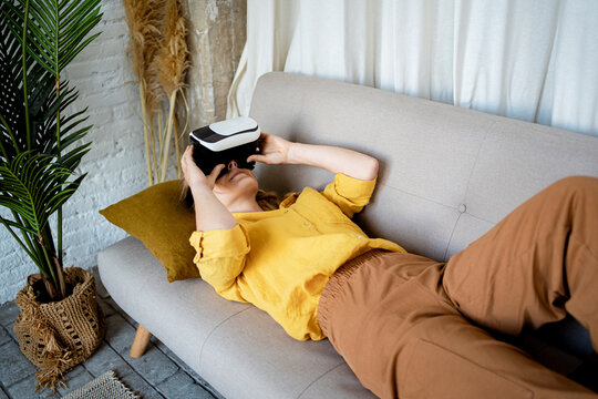 Woman using Virtual reality simulator while lying on sofa at home