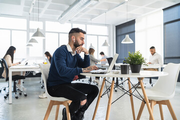 Male professional working on laptop with colleagues in background at coworking office