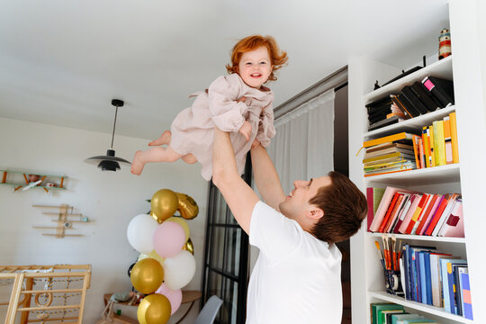 Smiling father picking up cute daughter by bookshelf at home