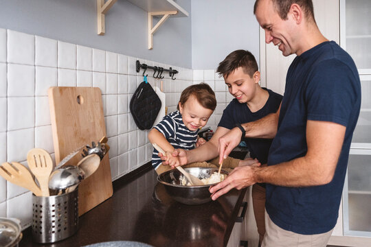 Cheerful sons helping father to prepare food in kitchen at home