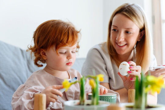 Smiling mother showing Easter egg to daughter at home