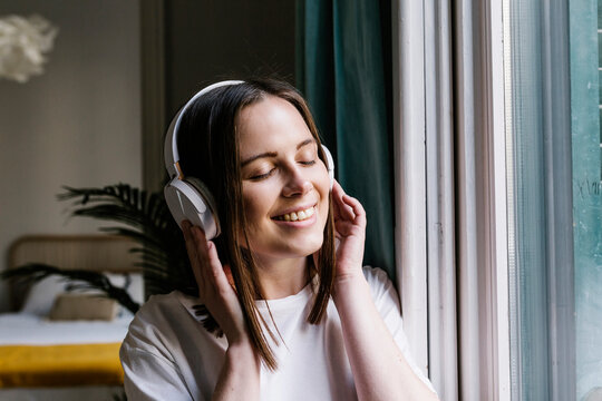 Woman smiling while listening music through headphones at home