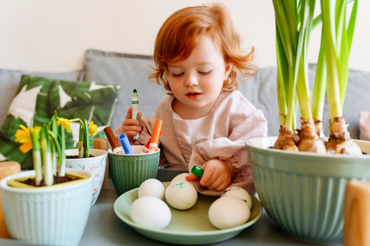 Cute girl looking at eggs in plate by potted plant during Easter