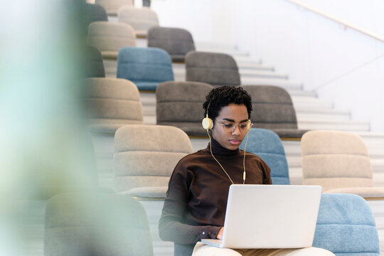 Young woman wearing headphones using laptop at auditorium