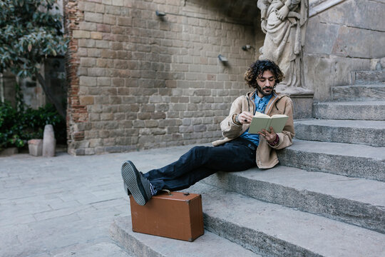 Young Man With Feet Up Reading Book While Sitting On Steps