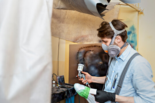 Shoemaker wearing gas mask while holding paint spray gun at workshop
