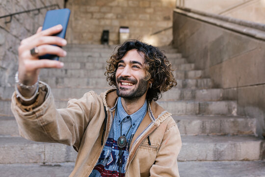 Happy hipster man taking selfie through mobile phone while sitting on steps