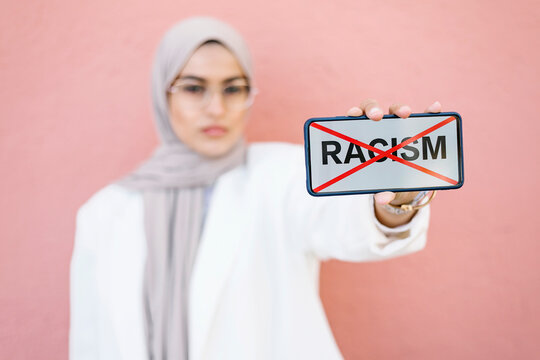 Young woman showing stop racism picture on smart phone in front of pink wall