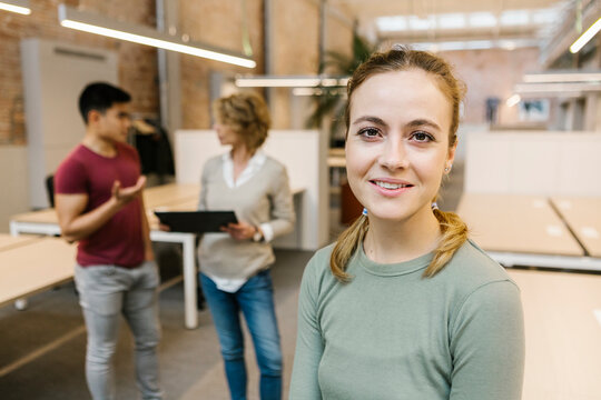 Businesswoman smiling with coworkers discussing in background at office