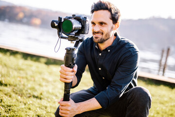 Handsome man holding gimbal looking through camera on sunny day