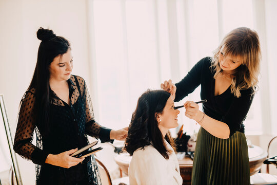 Female make-up artist and hairdresser preparing bride for wedding ceremony