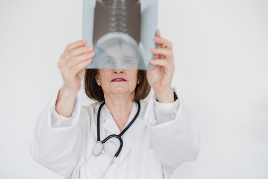 Senior female doctor examining x-ray image in front of white wall