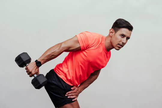 Male sportsperson bending while exercising with dumbbell by white wall - Powered by Adobe