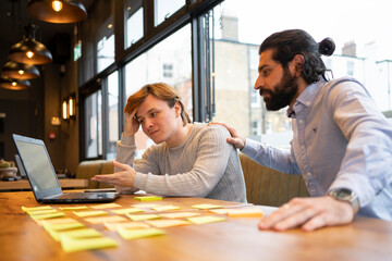 Worried young businessman discussing with coworker over laptop in office