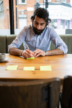 Handsome businessman writing on adhesive notes while working in coworking office