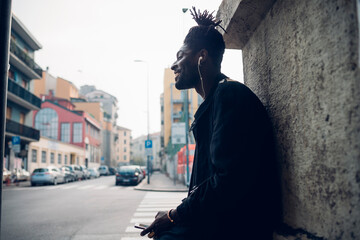 Smiling man listening music through in-ear headphones in city