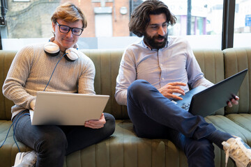 Male coworkers using laptop sitting on sofa at office