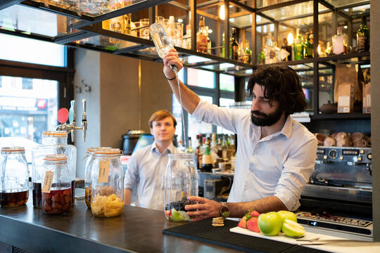 Male bartender pouring alcohol in fruit jar at bar counter