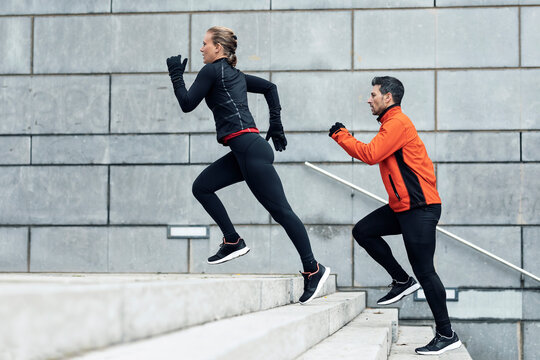 Athletic man and woman running up on steps by wall - Powered by Adobe