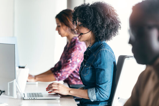 Female customer service representative using laptop while sitting amidst colleagues at office