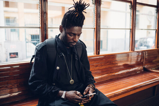 Young man with locs hairstyle using mobile phone sitting in tram