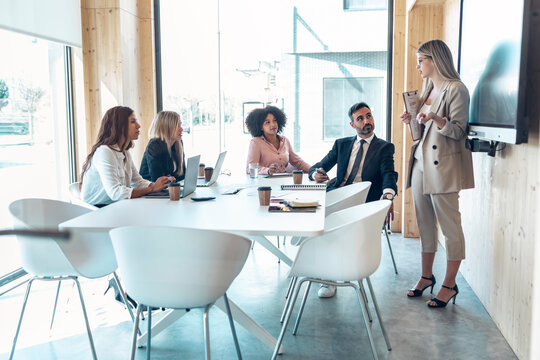 Female entrepreneur explaining to multi-ethnic coworkers in office