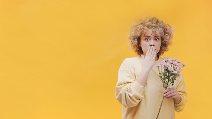 Shocked girl holding a bunch of purple gerbera daisies. Surprised expression. Attractive young girl with curly hair. Studio shot with a yellow background. High-quality photo. 