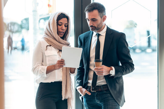 Businesswoman discussing with businessman over digital tablet at entrance of office