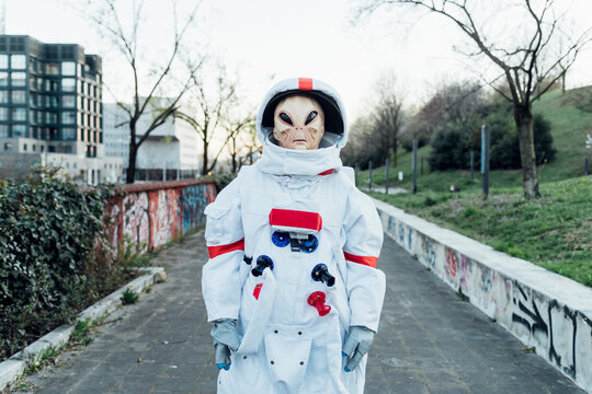 Young female astronaut with alien mask on footpath in city