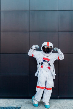Male astronaut flexing biceps in front of black wall