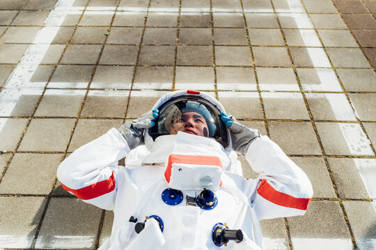 Young female astronaut in space suit lying down on footpath