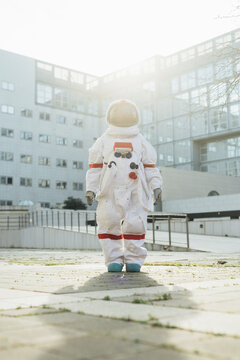Young female astronaut in space suit standing on footpath near building