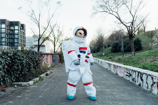 Female astronaut with alien mask standing on footpath