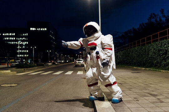 Female astronaut in space suit hailing ride while standing on footpath near road at night