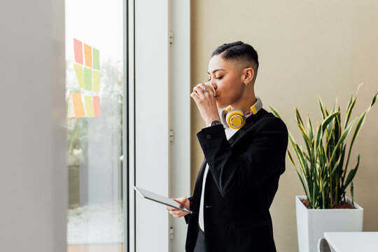 Female entrepreneur drinking coffee while standing with digital tablet at office - Powered by Adobe