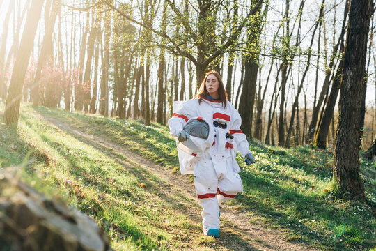 Young female astronaut holding space helmet while walking on dirt road